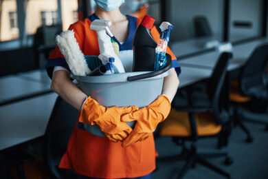 Cleaner in a face mask showing her cleaning products Cropped photo of a woman holding a plastic bucket with janitorial supplies with both hands