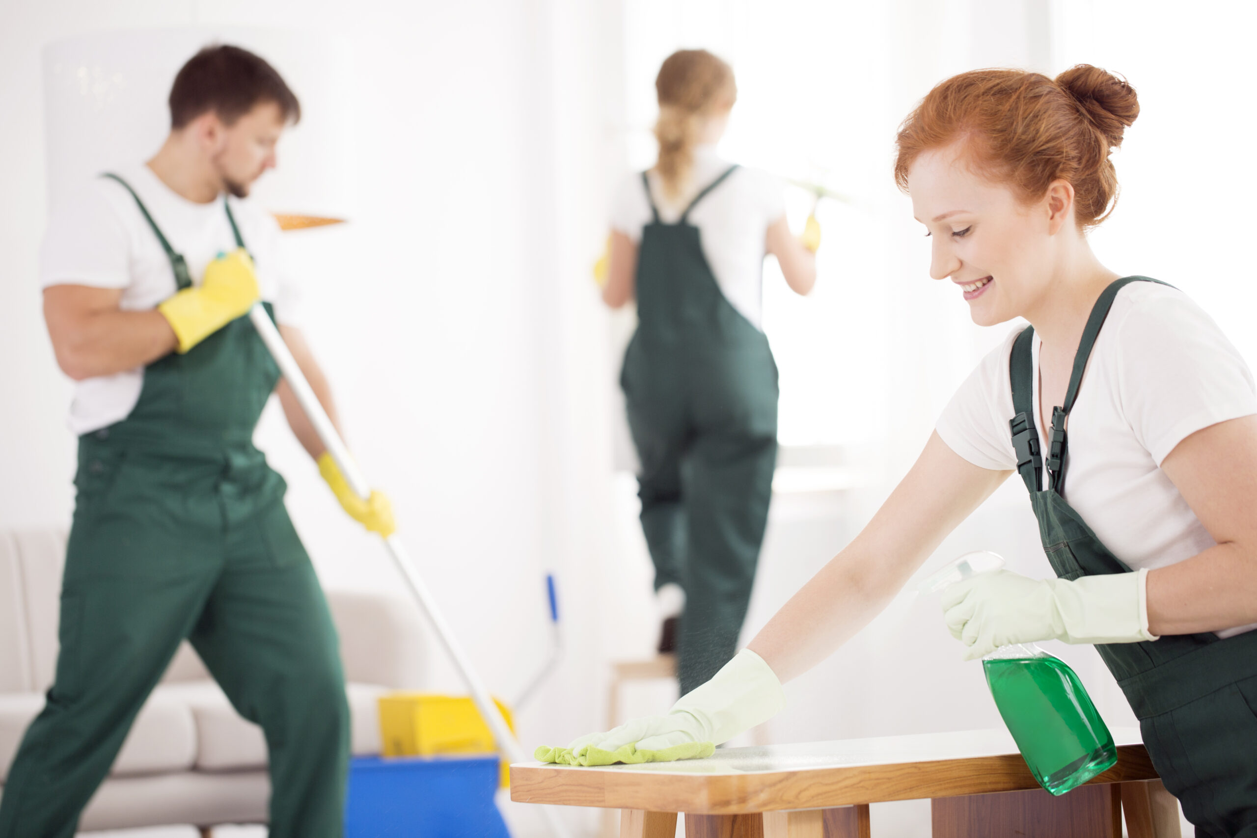 Cleaning service during work. Woman wiping a table while a man is washing the floor and other lady is cleaning the window