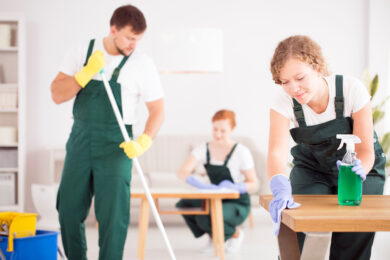 Woman in green overalls wiping table by using cleaning detergent