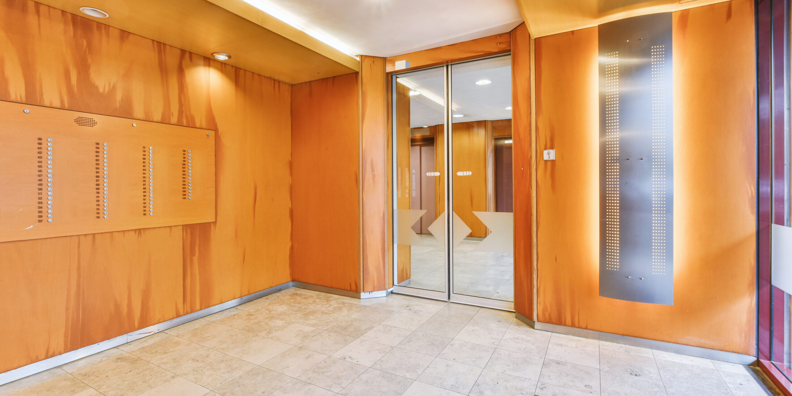 Shiny elevator with opened door located in illuminated hall of contemporary apartment building with tiled floor